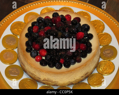 Käsekuchen mit Cranberries und Heidelbeeren obenauf, kreiste mit Schokoladen gold-Münzen des Euro. Stockfoto