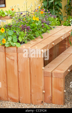 Holztisch mit Bänken im Hof Gemüsegarten mit Esswaren und Blumen in die Tischmitte. Stockfoto