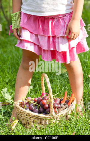 Mädchen stehen neben der Weidenkorb voller Trauben. Stockfoto