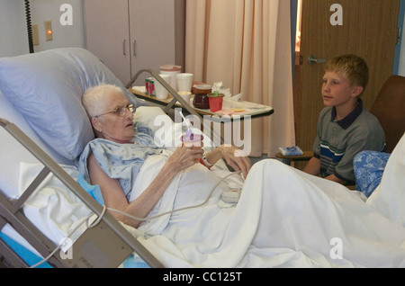 73 Jahre alte Anglo eingehakt mit Sauerstoff erhält Besuch von Enkel die lag sie im Krankenhausbett mit Krebs im Endstadium Stockfoto