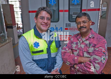 Zwei Männer, ein Feuerwehrmann und ein Sanitäter stellen Sie sich vor ihrer Feuerwache in Quito, Ecuador. Stockfoto