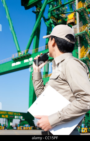 Männlichen Versand Industrie Arbeitnehmer spricht am Walkie-talkie mit Kran im Hintergrund Stockfoto