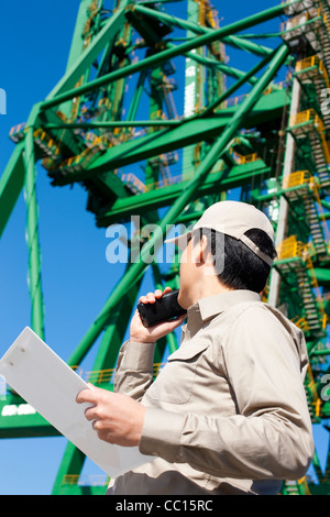 Männlichen Versand Industrie Arbeitnehmer spricht am Walkie-talkie mit Kran im Hintergrund Stockfoto