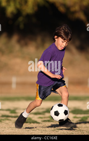 Junge im lila Hemd spielt Fußball in der späten Nachmittag Sonne Stockfoto