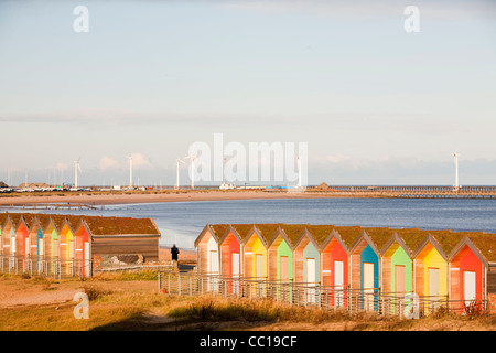 Bunte traditionelle britische Küste Strandhütten am Strand in Blyth, Nord-Ost, UK, mit Windkraftanlagen hinter. Stockfoto