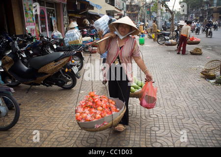 Eine Frau trägt einen Korb mit Früchten aus dem Markt zu verkaufen auf der Straße auf einem Schulter-Mast, Ho-Chi-Minh-Stadt, Vietnam Stockfoto