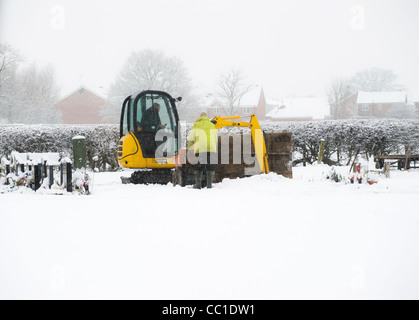 Totengräber graben mechanisch ein Grab mit einem kleinen Bagger auf dem schneebedeckten britischen Friedhof an einem Wintertag. VEREINIGTES KÖNIGREICH Stockfoto
