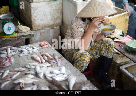 Eine Frau isst Frühstück an ihrem Stand Meeresfrüchte in Hoi an einem Fischmarkt, Vietnam Stockfoto