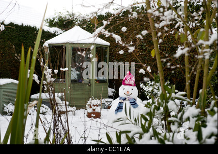 Schneebedecktes Gewächshaus mit Schneemann im Vordergrund eines britischen Gartens im Winter. Stockfoto