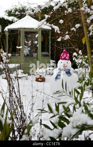 Schneebedecktes Gewächshaus mit Schneemann im Vordergrund eines britischen Gartens im Winter. Stockfoto