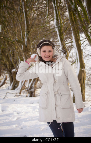 Junge kaukasische Hündin in einem schneebedeckten Wald blickt lächelnd auf die Kamera und ist dabei, einen Schneeball zu werfen Stockfoto