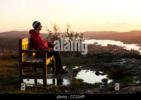 Ein Mann sitzt auf einem Denkmal Sitz auf Orrest Head oben Windermere im Lake District, Cumbria, England. Stockfoto