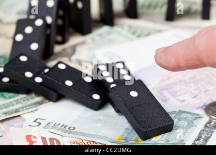Finger schieben gefallenen Dominos auf Pfund, Euro und Dollar-Banknoten, die zur Veranschaulichung Bankenkrise Stockfoto