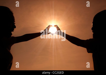 glückliches junges Paar machen Herzform mit Händen bei Sonnenuntergang Stockfoto