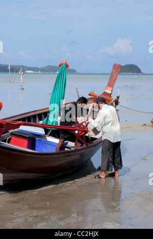 Zwei asiatische Fischer arbeiten auf ein Longtail Fischerboot sind gefesselt an einem Strand in Chalong Bay, Insel Phuket, Thailand. Stockfoto