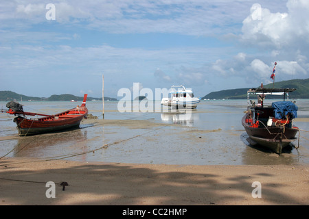 Longtail Fischerboote sind an einem Strand bei Ebbe in Chalong Bay, Insel Phuket, Thailand gefesselt. Stockfoto