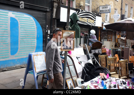 Ein Brick Lane Market Trader flirtet mit einem Kunden, die in die Reflexion des Spiegels gesehen werden kann Stockfoto