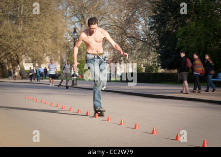 Inline-Skater demonstriert seine Fähigkeiten auf einer Slalomstrecke, während Passanten am Hyde Park, London sehen. Stockfoto