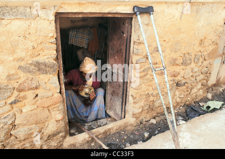 Ein armer Mann (mit einer Krücke) isst in seinem kleinen Zimmer, die mit Blick auf die Straße (Indien) Stockfoto