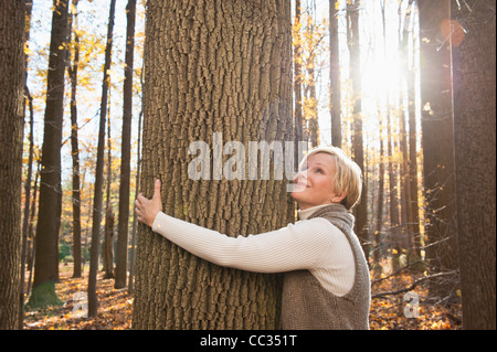 USA, New Jersey, Smiling Frau umarmt Baum im Herbst Wald Stockfoto