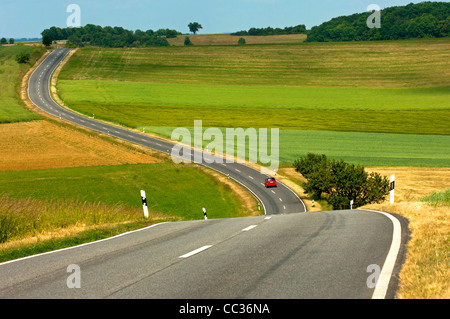 Landstraße schlängelt sich durch Felder in einer hügeligen Landschaft, Rheinland-Pfalz, Deutschland Stockfoto