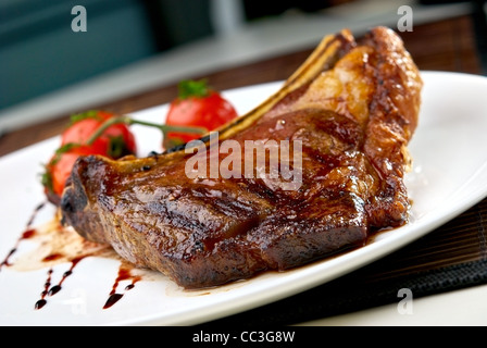 Club-Steak. Kalbfleisch auf den Knochen. Gegrilltes Fleisch Rippen auf weißen Teller mit Cherry-Tomaten und dunklen hot sauce Stockfoto