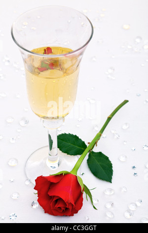 Foto von einer einzelnen roten Rose und ein Glas Champagner mit gefälschten Diamanten Tabelle Konfetti. Schwerpunkt ist die Rose. Stockfoto