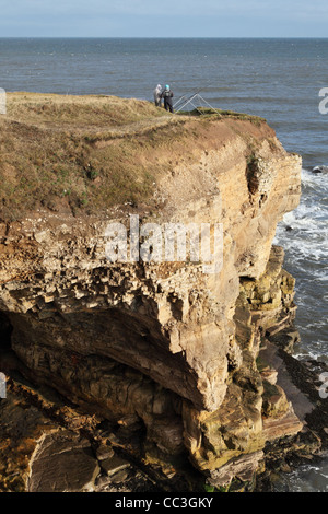 Zwei Männer Linie Fischerei vor gefährlichen Klippen an der Nordsee-Küste in der Nähe von South Shields, Nord-Ost England UK Stockfoto