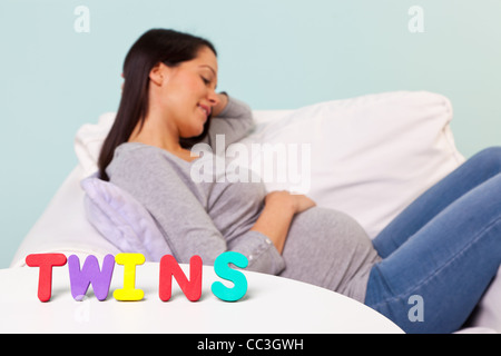 Foto von einer schwangeren Frau zu Hause sitzt in einem Sessel, Konzentration auf das Wort Zwillinge auf dem Tisch vor. Stockfoto