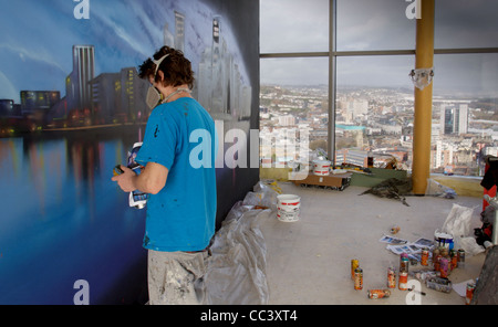 Ein maskierter Graffiti-Writer arbeitet auf eine groß angelegte Wandbild in einem Hochhaus mit Blick über die Stadt von Swansea sichtbar Stockfoto