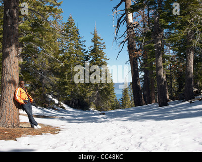 Ein Mann lehnt sich an eine Tanne mit Schnee überall auf dem Boden Stockfoto