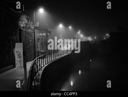 Ein frost Gehweg, Wanderwege entlang eines Kanals unter Lampen durch Nebel gedimmt. den Kanal diese Lichter in der Ferne zurückweichenden spiegelt Stockfoto