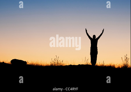 Mann mit erhobenen Armen in der indischen Landschaft in der Dämmerung. Silhouette Stockfoto