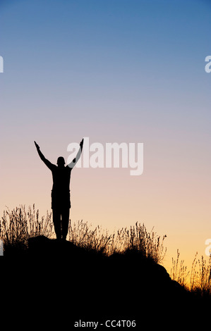 Mann mit erhobenen Armen in der indischen Landschaft in der Dämmerung. Silhouette Stockfoto