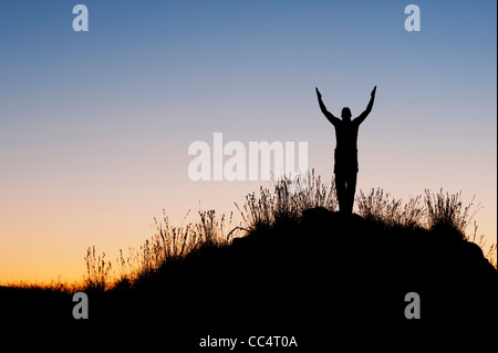 Mann mit erhobenen Armen in der indischen Landschaft in der Dämmerung. Silhouette Stockfoto