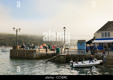 Fowey, Cornwall, England, Vereinigtes Königreich, Großbritannien. Menschen am Fluss Quai mit Meer Nebel clearing über die Hügel Stockfoto