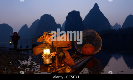 Kormoran Fischer tendenziell Laterne mit Vögel auf Bambus-Floß in der Morgendämmerung mit Karst-Gipfel am Ufer des Flusses Li Yangshuo China Stockfoto