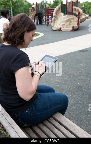 Kaukasische Frau sitzt auf einer Parkbank, ihrem iPad lesen Stockfoto