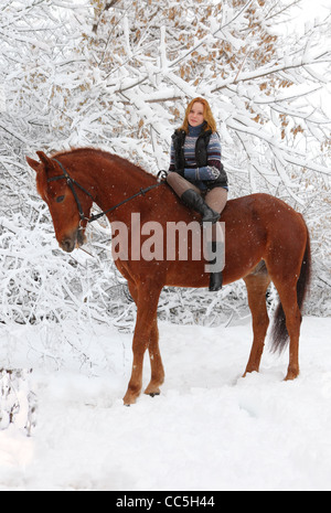 Blonde 22-jährige Model Mädchen posiert mit ihrem Pferd in einer Schneelandschaft, Fokus auf das Mädchen Stockfoto