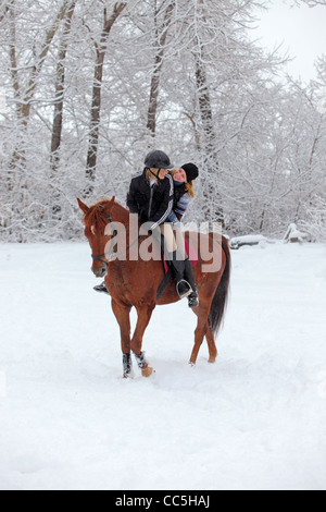 Zwei blonde 22-Jahre Mädchen mit ihrem Pferd in einer Schneelandschaft, konzentrieren sich auf das Mädchen Stockfoto