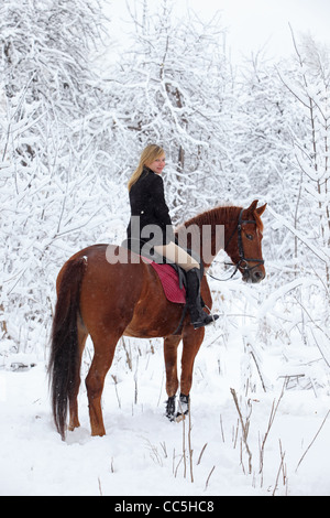 Blonde 22-jährige Mädchen mit ihrem Pferd in einer Schneelandschaft, konzentrieren sich auf das Mädchen Stockfoto