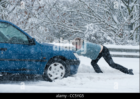 Eine Dame versucht, ihr Auto zu schieben, nachdem es im Schnee stecken Stockfoto