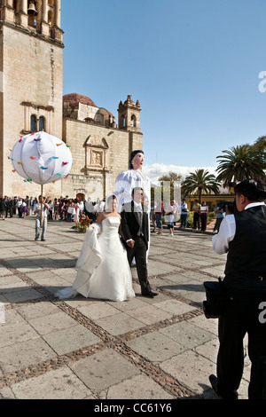 elegante mexikanische Braut & Bräutigam überqueren Plaza außerhalb der Kirche von Santo Domingo nach Trauung, gefolgt von Fahnenträger Stockfoto