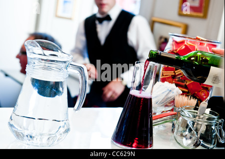 Ein Kellner schaut zu, wie ein roten Sieg in eine Karaffe neben einen Krug Wasser gegossen wird Stockfoto