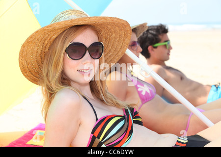 Junge Frau in einem Strohhut, Sonnenbaden am Strand mit Freunden Stockfoto
