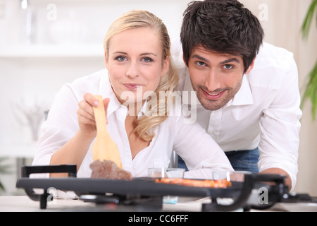 Paar, Kochen, Steak und Gambas auf einer Tischplatte Kochplatte Stockfoto