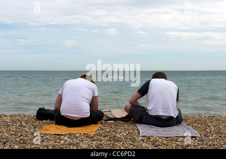 Die Rückseiten der beiden jungen Männer sitzen auf Handtücher für den Strand in Brighton Stockfoto
