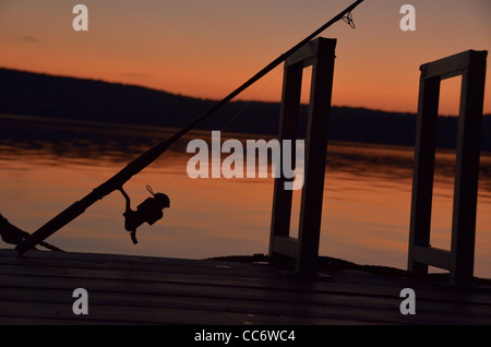 Eine Angelrute ruht auf einem Dock mit einem wunderschönen Sonnenuntergang im Hintergrund. Stockfoto