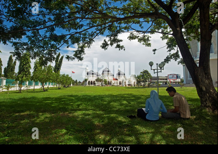 Indonesien, Sumatra, Banda Aceh, paar unter Baum vor Moschee Baiturrahman (Mesjid Raya Baiturrahman) Stockfoto