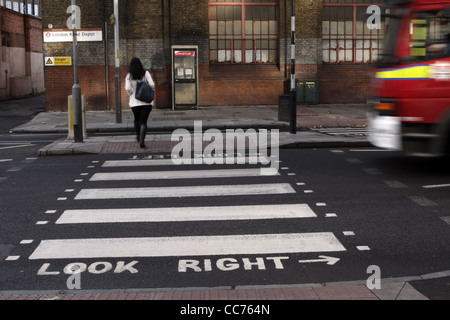 eine Frau geht über einen Zebrastreifen in London, während hinter ihr ein Fahrzeug beschleunigt Stockfoto